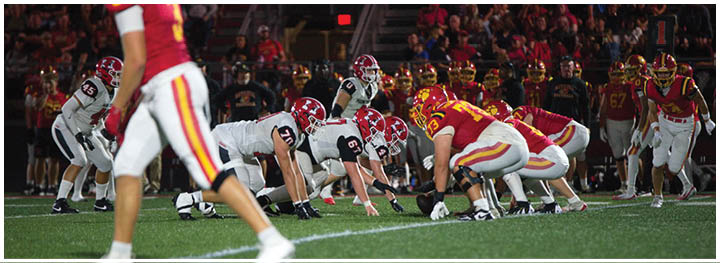 Two opposing American football teams are lined up facing each other on the field, ready for the next play, with players in red and white uniforms. Description generated by AI