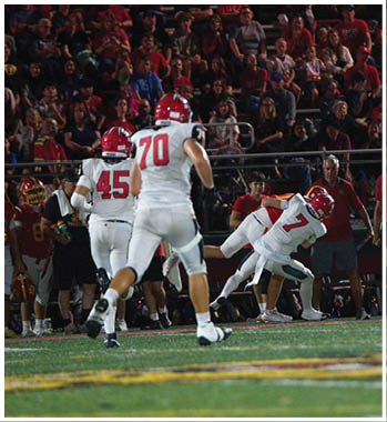 People in football uniforms are on a field with a large crowd of spectators in the background during a nighttime game. Description generated by AI