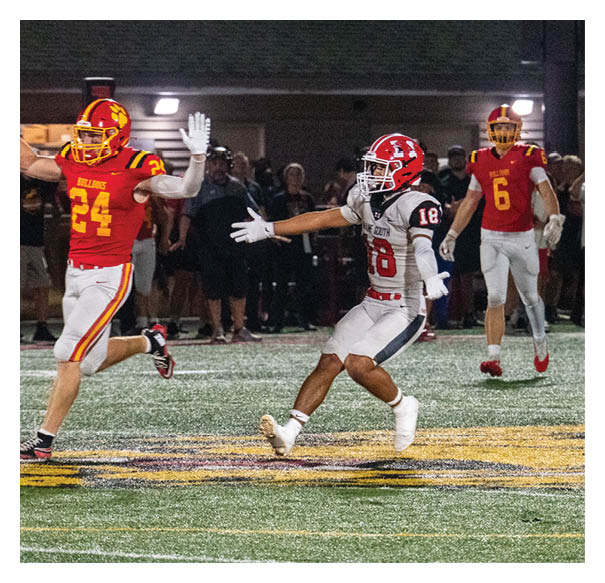 Two opposing football teams wearing red helmets and black and white uniforms are lined up facing each other on a green field preparing for a play. Description generated by AI