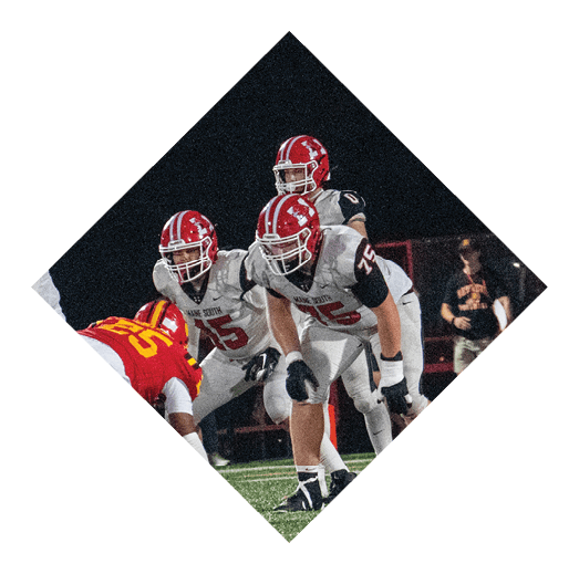 A person wearing a red helmet and black sports uniform is running on a football field while holding a football, preparing to throw it. Description generated by AI