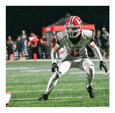People wearing helmets and football uniforms are actively playing on a grassy field with one person running with the ball while others attempt to block or tackle. Description generated by AI