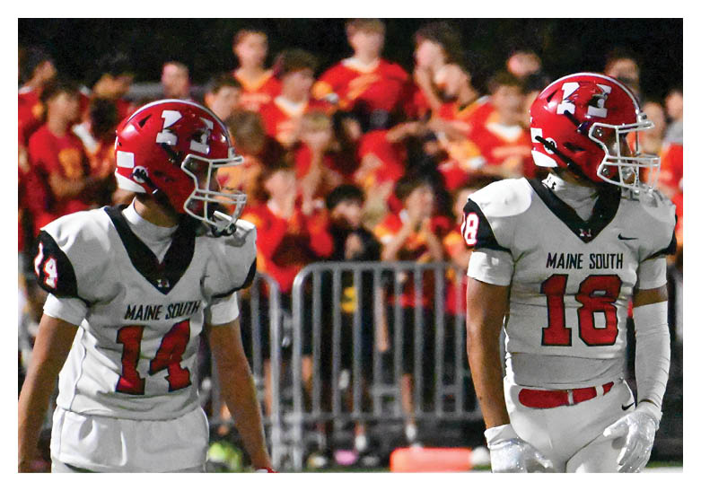 Players in red helmets and black and white uniforms are lined up on a football field preparing for a play during a game. Description generated by AI