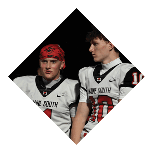 Several people wearing red helmets and sports uniforms are positioned on a football field preparing for a play. Description generated by AI