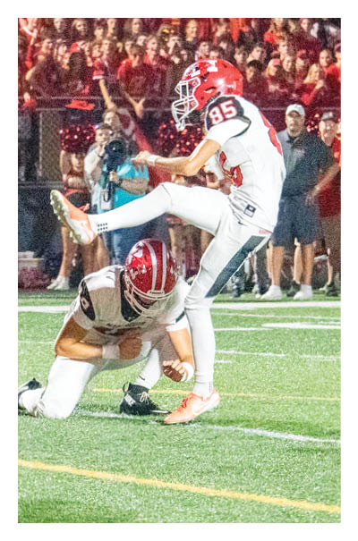A person wearing a red helmet and white jersey with the number one is preparing to throw a football while other players and a referee stand nearby on a football field. Description generated by AI