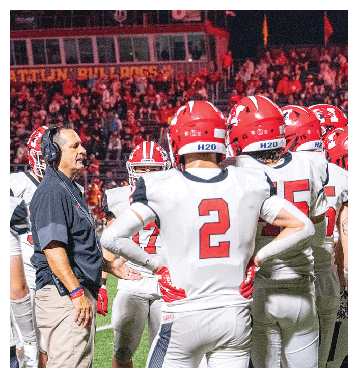 Several people wearing red helmets and football uniforms are positioned on a football field preparing for a play. Description generated by AI