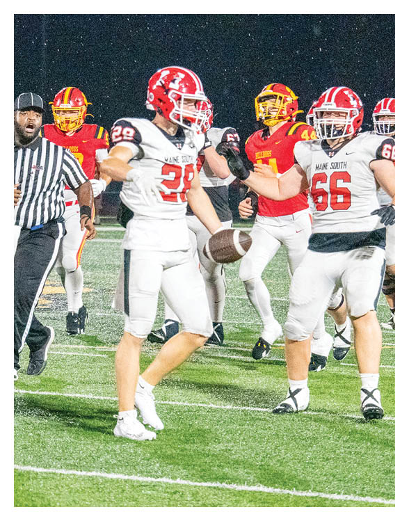People wearing sports uniforms and cleats are standing on a football field near the 20-yard line. Description generated by AI