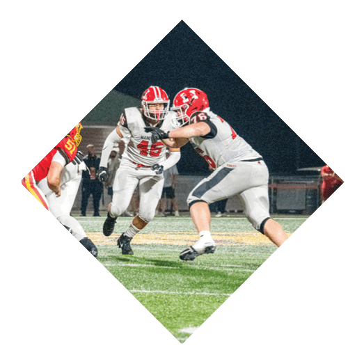 Three people wearing football uniforms and helmets are engaged in a tackle on a green football field. Description generated by AI