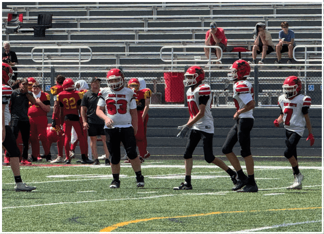 Children wearing helmets and football uniforms are engaged in a blocking drill on a grassy field. Description generated by AI