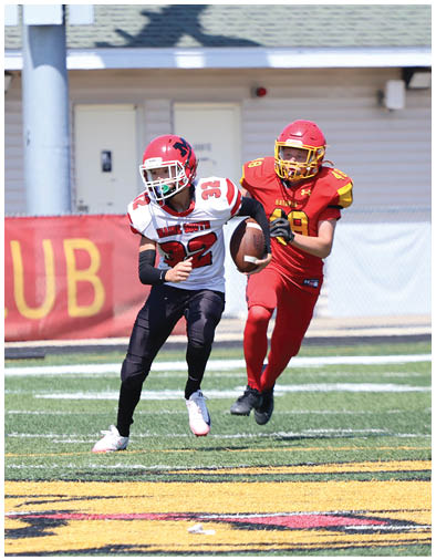 A group of people in red and yellow football uniforms are playing on a field with one person in a white and black uniform running with the ball while others attempt to catch them. Description generated by AI