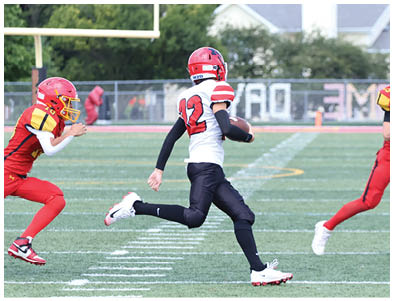 Three people in football uniforms are running on a field with one person in a white jersey holding a football while two others in red jerseys chase. Description generated by AI