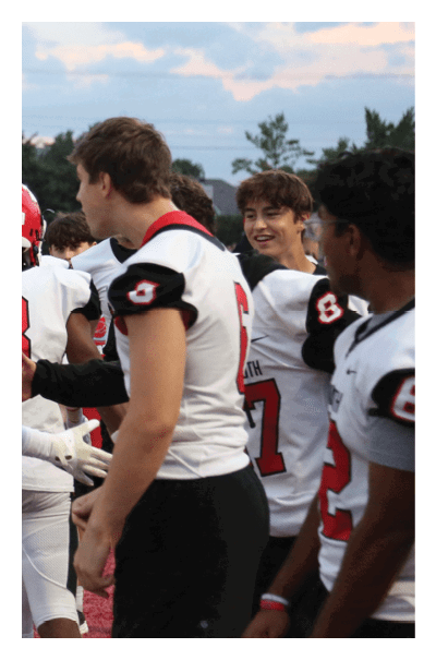 People wearing football uniforms are standing on a field with yard lines visible. Description generated by AI