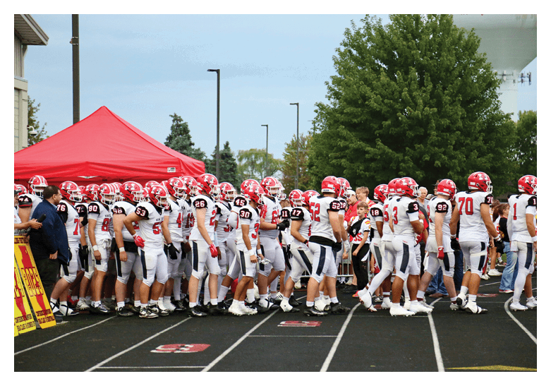 A group of people wearing white and red football uniforms are walking together on a track near a red tent. Description generated by AI