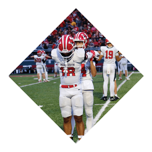 Two people in football uniforms stand on a field with one person raising their arms while the other stands behind them. Description generated by AI