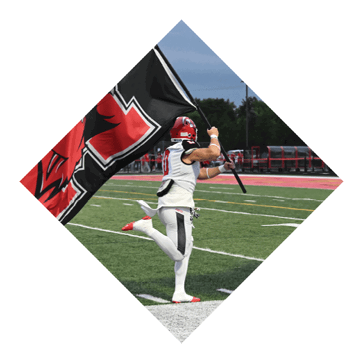 A person in a football uniform is running on a field while holding and waving a large black flag with a red and white design. Description generated by AI