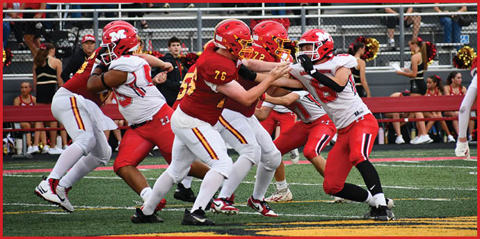 Adults wearing football uniforms in red and white are engaged in a blocking play on a football field during a game. Description generated by AI