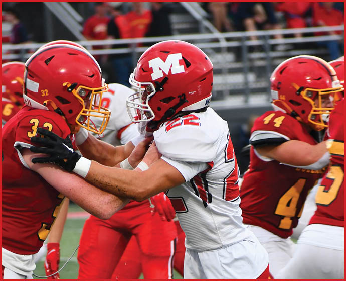 Two people in football uniforms and helmets are engaged in a physical play on the field with others in the background. Description generated by AI
