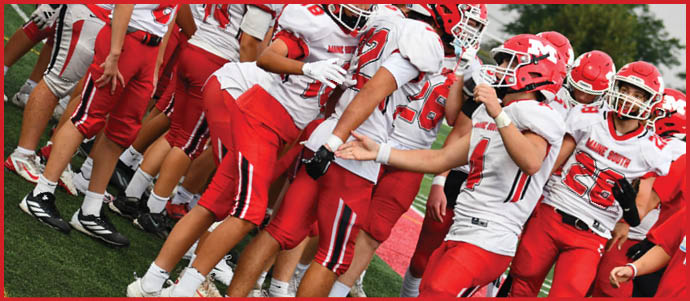 A group of people wearing red and white football uniforms are standing closely together on a grassy field, appearing to celebrate or prepare for a game. Description generated by AI