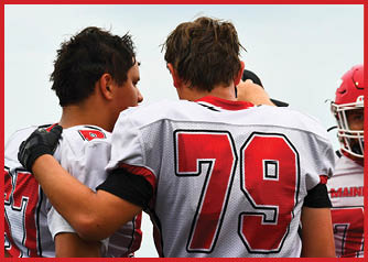 Two people wearing white and red football uniforms are standing close together with one person’s arm around the other’s shoulder. Description generated by AI
