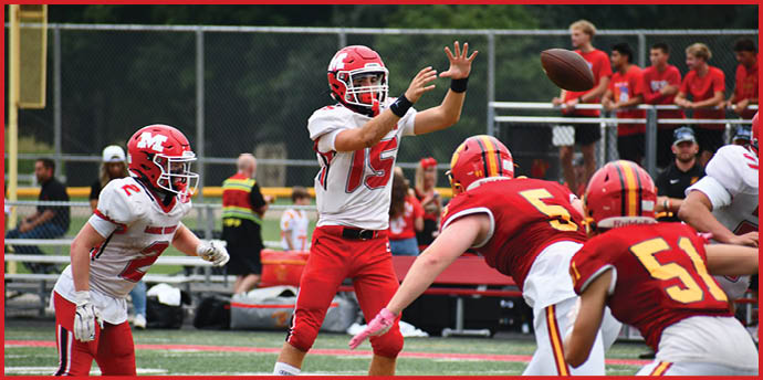 A group of people in football uniforms are on a field with one person in white and red preparing to throw a football while others in red and yellow uniforms are positioned defensively. Description generated by AI