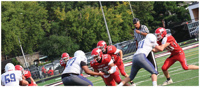 People in red and white football uniforms are engaged in a play on a green field with trees and a referee in the background. Description generated by AI