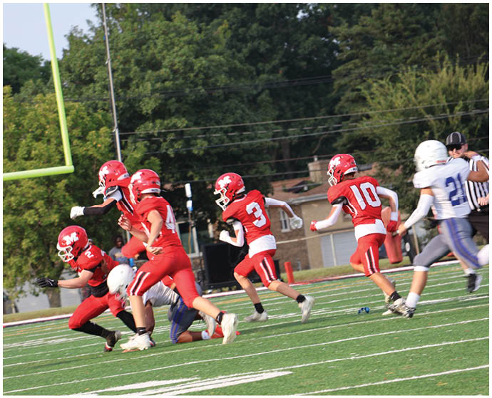 Several people in red football uniforms are running on a green field with white yard lines and a yellow goalpost in the background. Description generated by AI