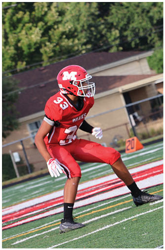 A person wearing red athletic pants and black cleats is running on a green football field near the 20-yard line marker. Description generated by AI