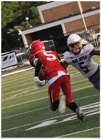 A person in a red football uniform is running with the ball while another person in a white uniform is attempting to catch them on a football field. Description generated by AI