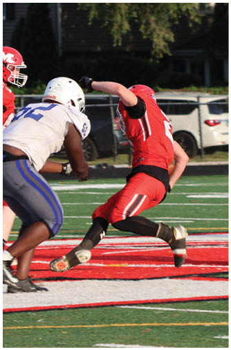 Two people in football uniforms are engaged in a play on a field with one person in red diving or falling near the end zone while the other in white approaches. Description generated by AI