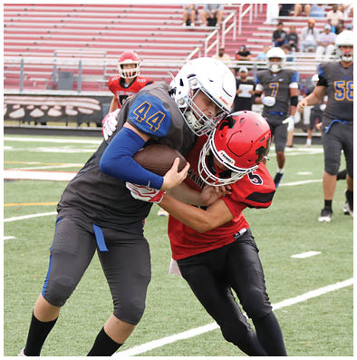 Two people in football uniforms are engaged in a tackle on a field with one holding the ball tightly. Description generated by AI