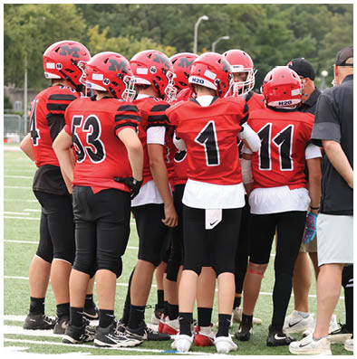 People wearing red sports jerseys with numbers and black athletic pants are standing closely together on a field. Description generated by AI