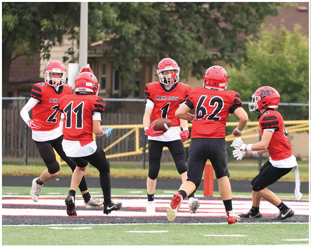 Three people wearing red and black football uniforms are on a field, with one person holding a football and the others preparing to catch or block. Description generated by AI