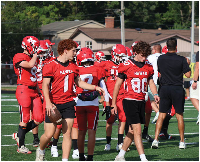 Several people wearing red sports jerseys and shorts are standing on a grassy field, with one person holding a football. Description generated by AI