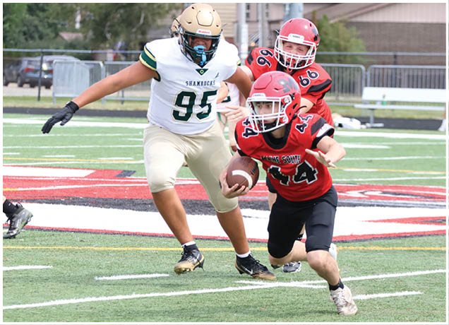 A person in a red football uniform is running with the ball while two people in white and red uniforms chase on a football field. Description generated by AI