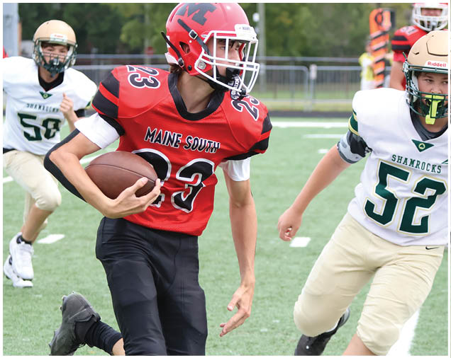 Two people in sports uniforms are running on a football field, with one holding a football and the other attempting to catch up. Description generated by AI