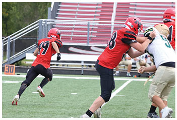 A person wearing a red sports jersey and black pants is running on a green football field near a marker displaying the number 30. Description generated by AI