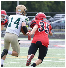 Two people in football uniforms are running on a field with one person in a white and gold uniform holding a football while being pursued by two people in red and black uniforms. Description generated by AI