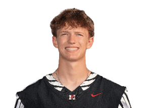 A person with short curly hair is smiling and wearing a black sports jersey with the word “HAWKS" and a red Nike logo. Description generated by AI