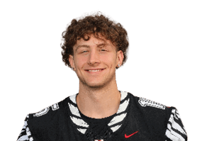 A person with curly hair is smiling and wearing a black sports jersey with white details. Description generated by AI