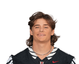 A person with medium-length wavy hair is smiling and wearing a black sports jersey with white and red accents. Description generated by AI