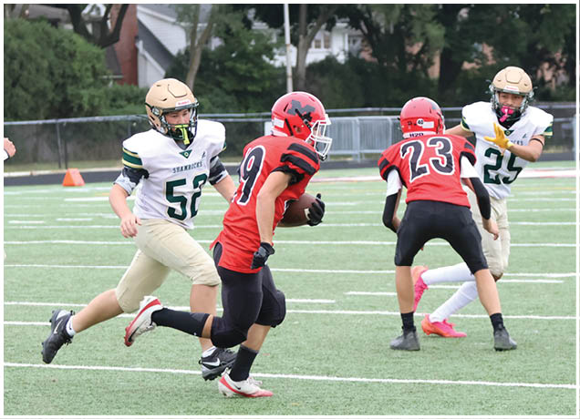 Several people wearing football uniforms are actively running on a green field during a game, with some players in red and others in white and gold. Description generated by AI