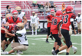 People wearing red and white football uniforms are playing on a field with some players tackling and others running. Description generated by AI