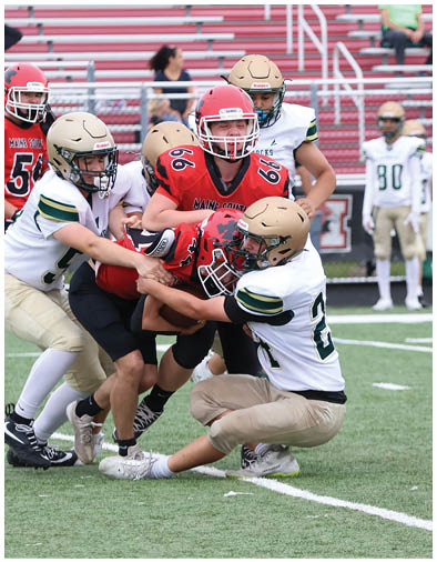 A group of people in football uniforms are engaged in a tackle on a field with bleachers and spectators in the background. Description generated by AI