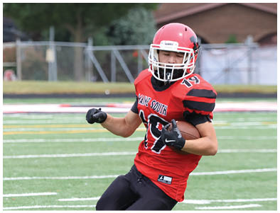 A person wearing a red and black football uniform is running on a green football field. Description generated by AI