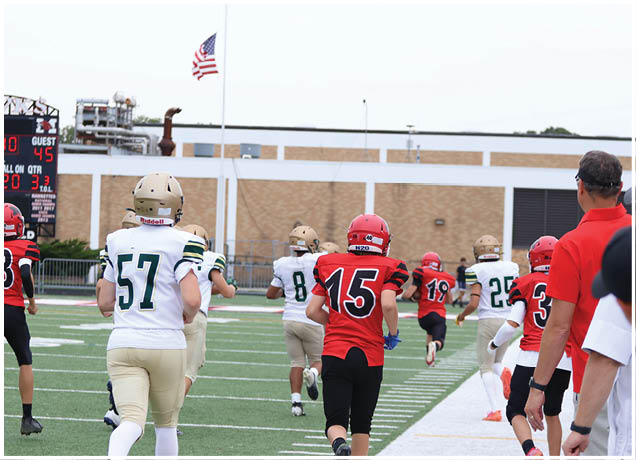 Players in football uniforms are running on a field toward the end zone with a scoreboard showing the score and time in the background. Description generated by AI