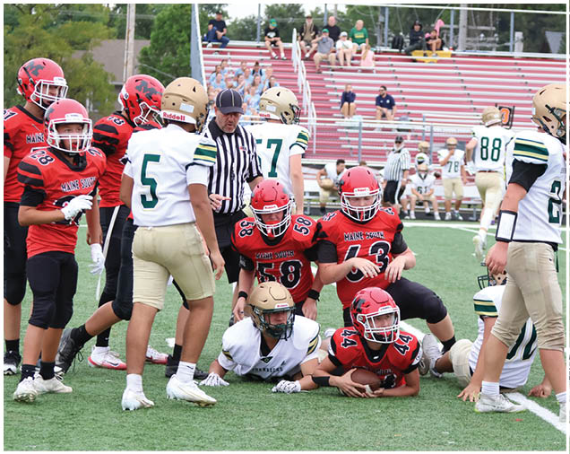 A group of people wearing football uniforms are gathered on a field with some players standing and others on the ground during a game. Description generated by AI