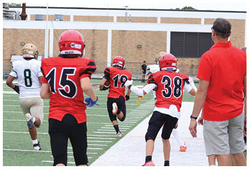 People wearing football helmets and uniforms are running on a football field toward the end zone. Description generated by AI
