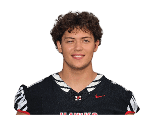 A person with curly hair is wearing a black sports jersey with the word “HAWKS" in red and white letters and smiling against a white background. Description generated by AI