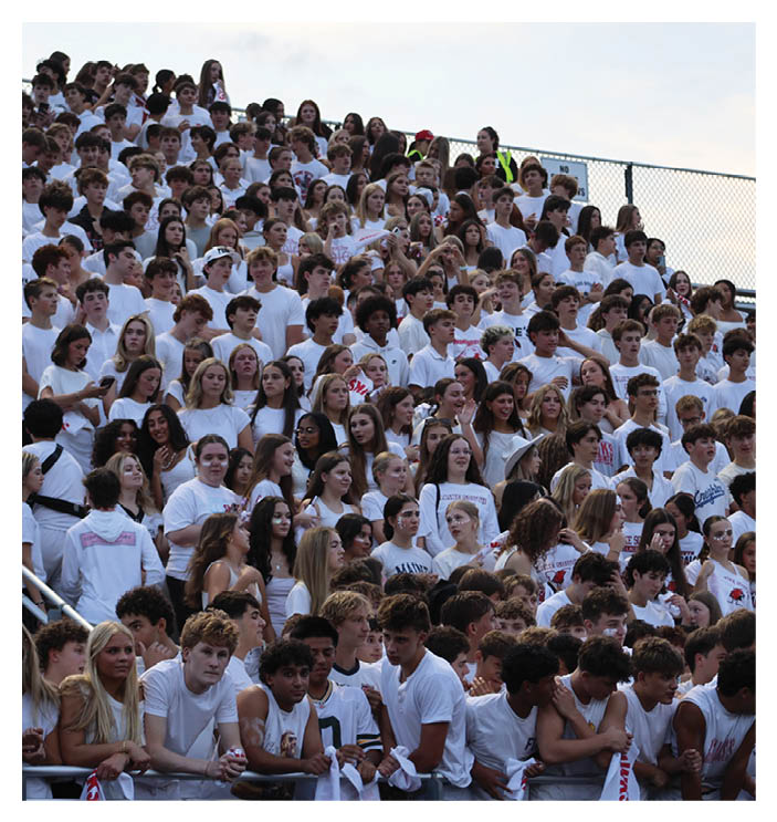 A large crowd of people wearing mostly white shirts are gathered closely together in bleachers, appearing to be at an outdoor event or sports game. Description generated by AI