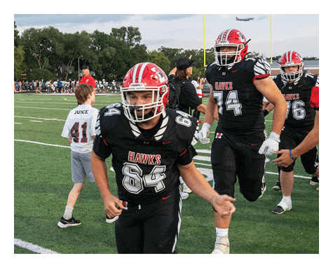 Adults wearing football uniforms with red and black colors are on a football field, some running and others standing near the goalposts. Description generated by AI