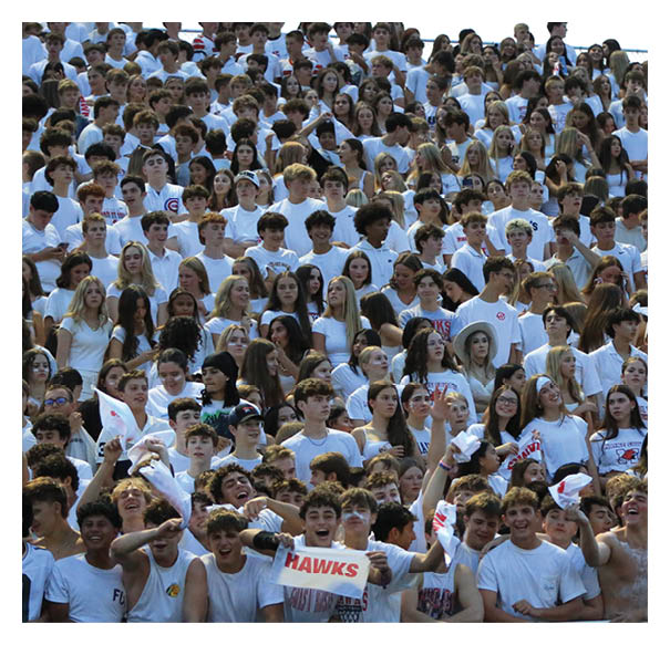 A large crowd of people wearing white shirts is gathered closely together in bleachers, some holding signs and waving white towels, appearing to cheer at a sports event. Description generated by AI